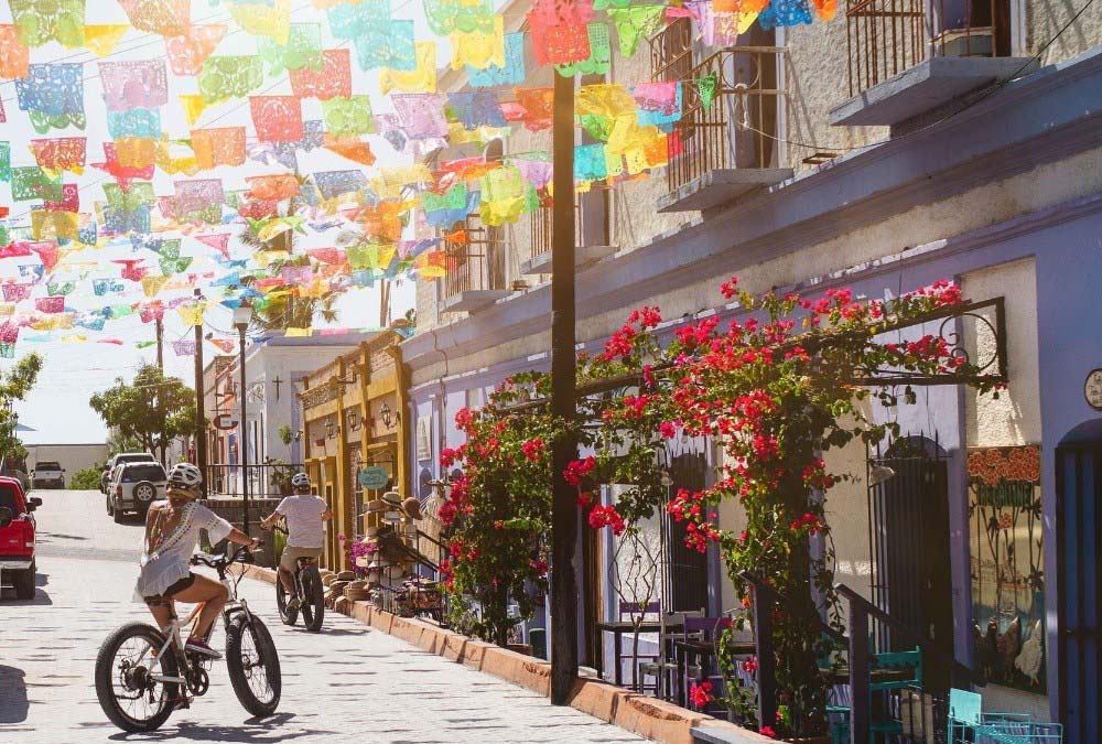 Calle de Todos Santos con flores y vistas a tiendas y personas en bicicleta